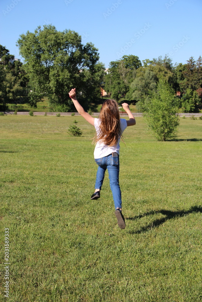 Fototapeta premium Happy Young Girl Jumping in the Air on a Green Grass Field
