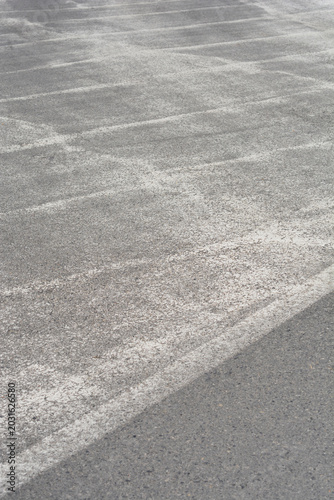 An eye level perspective shows a worn gray asphalt surface covered with patterns of fading white traffic markings or paint.