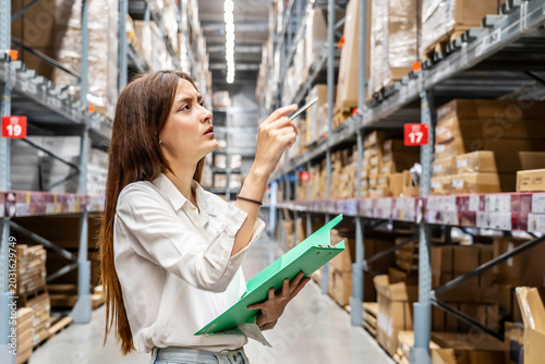Bild auf Leinwand Large storage facility, Young woman diligently checking her clipboard as she org