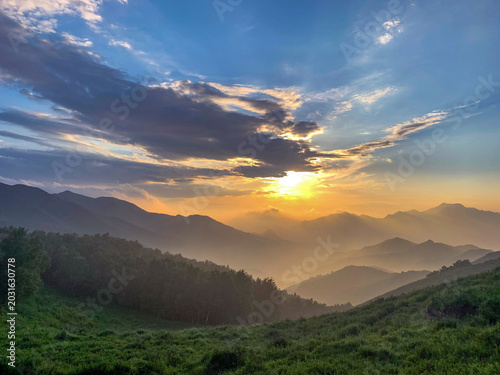 Foto Breathtaking sunset over rolling green mountains with scattered clouds