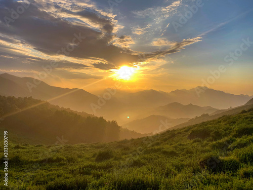 Foto Sunrise over mountainous landscape with green grass and clouds