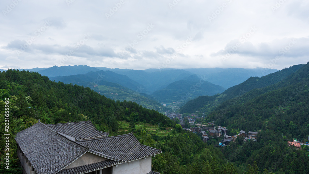 Obraz premium Scenic mountain view of Xijiang Miao Village, Guizhou, China with traditional roof and cloudy sky.