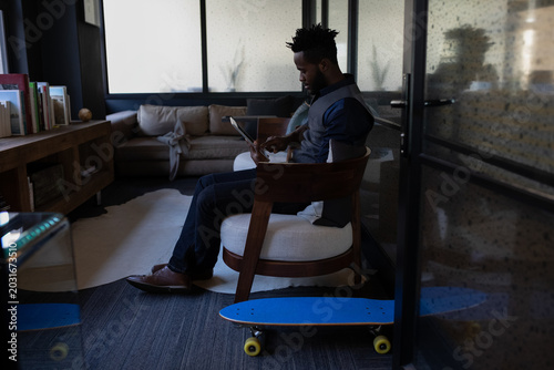 Blue skateboard with yellow wheels is resting on floor in low-lit office lounge near armchair