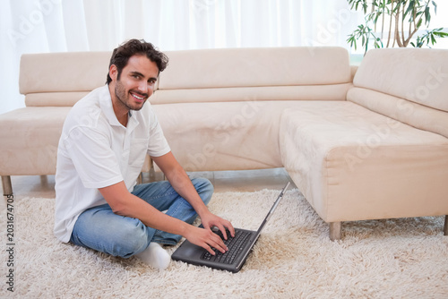 Foto Mid-adult man sitting cross-legged on shag rug in living room using black laptop