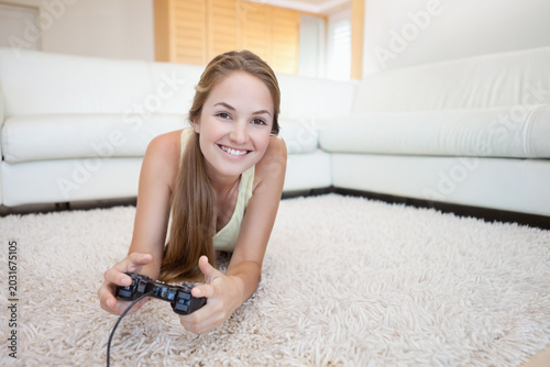 Tableau sur toile Female lying on stomach on light shag rug in living room holding wired game cont