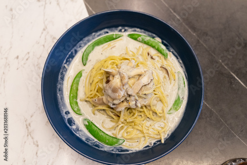 A blue plate features creamy truffle pasta coated in a rich white sauce with black pepper and truffle toppings. Bright green peas provide contrast and freshness to the elegant dish. The composition em