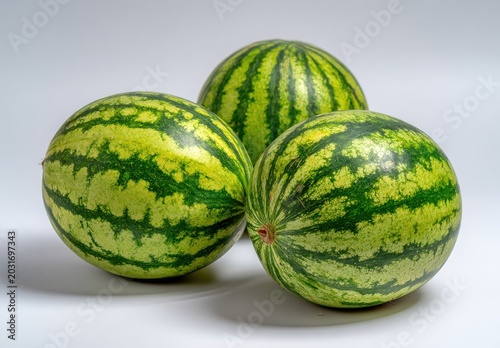 Three whole watermelons on a white surface with green and yellow stripes