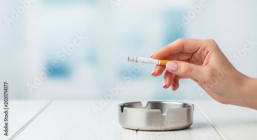 Close-up of a hand holding a lit cigarette over a metal ashtray, symbolizing smoking habit