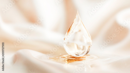 A luxurious cosmetic serum or oil drop on a soft beige silk fabric, a transparent golden drop of water with gentle waves and an elegant textile background.