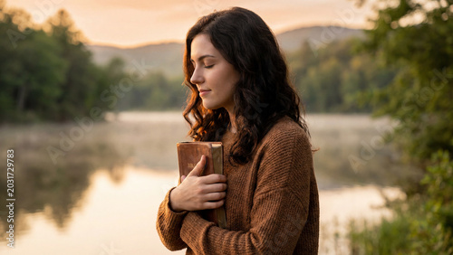 A serene young woman praying with her Bible by a misty lake at sunrise, embodying faith, hope, and spiritual reflection