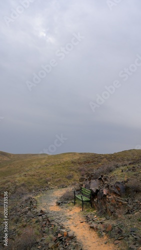 Solitary bench on a stony trail through desolate hills under cloudy skies