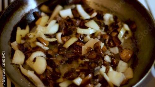 Fresh sliced mushrooms and onions being fried in a hot metal pan on a stove