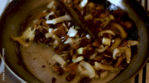 Fresh sliced mushrooms and white onions being fried in a hot pan on a kitchen stove