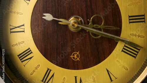 Vintage antique clock ticking fast with golden roman numerals and wooden background