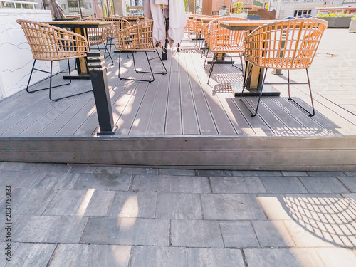 Outdoor cafe patio with wooden tables and rattan chairs. Empty restaurant terrace on a wooden deck. Alfresco dining setup