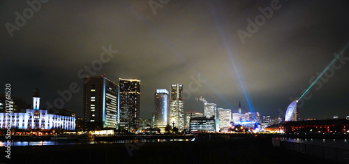 Schilderij op canvas 夜の横浜みなとみらい21地区を望む美しい夜景で赤レンガ倉庫やインターコンチネンタルホテルなどのランドマークがライトアップされ夜空にサーチライトが放たれる幻想的な