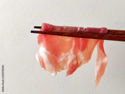 Thinly sliced pork neck for shabu-shabu, with chopsticks lifting the pieces against a white background.