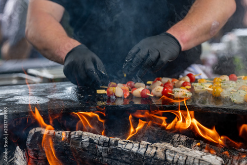 Préparation de brochettes de fruits de mer sur brasero avec cuisson au feu de bois et fumée en extérieur.