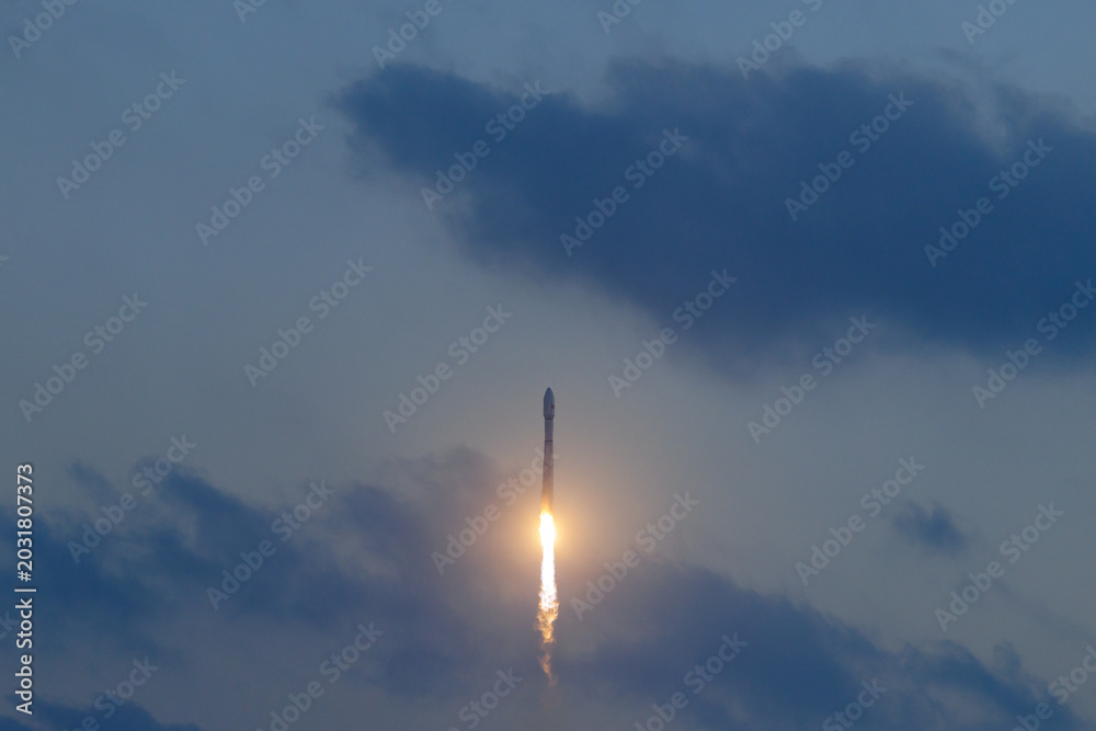 Fototapeta premium Rocket launching into cloudy sky at dusk with bright flame trail, aerospace program of China
