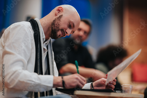 Cuadro en lienzo A bald man leans over a notepad as he writes with a pen during a meeting