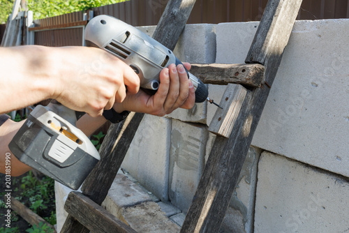 Photos A close-up of a person using a cordless drill to fix a wooden ladder rung agains