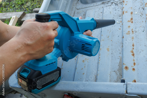 A high-angle shot of a person using a blue cordless blower to clean the rusty metal bed of a trailer