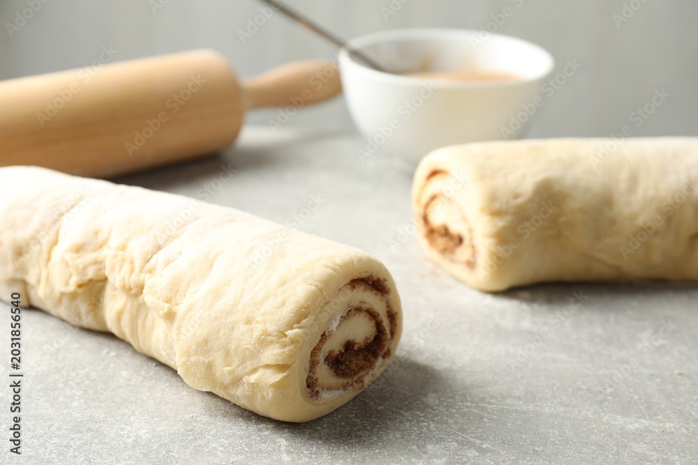 Fototapeta premium Raw cinnamon roll dough on grey textured table, closeup