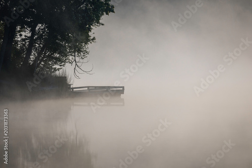 Aufnahmes eines Angelstegs im Morgennebel an einem See.
