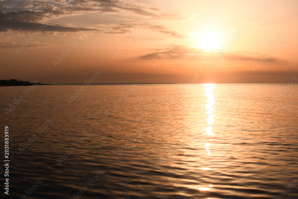 Obraz premium Sunset over calm ocean with warm orange colors reflecting on water surface. peaceful scene, sense of tranquility and nature beauty. Beautiful sunset on calm sea.golden sunlight shimmering across water
