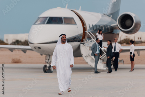 Tableau sur toile Businessman in traditional Middle Eastern attire walking from private jet with c