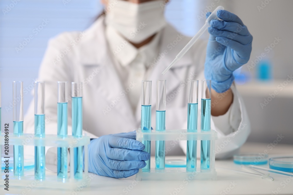 Fototapeta premium Scientist dripping blue liquid into test tube at white table in laboratory, closeup