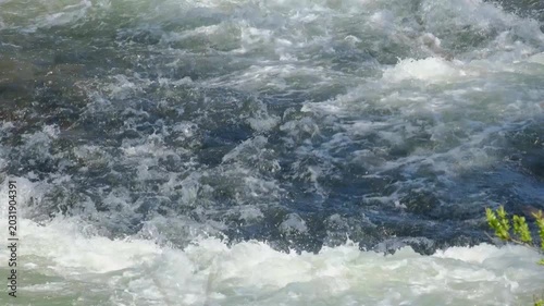 A close-up of a turbulent river with white foam and waves.