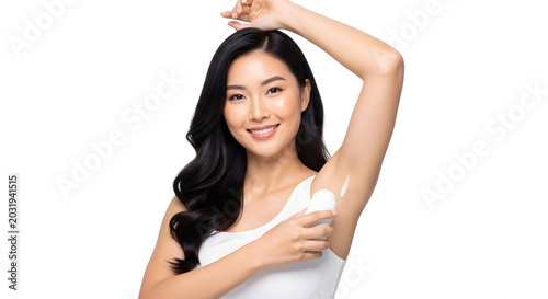 Underarm Care: A beautiful Asian woman with long, dark hair applies antiperspirant to her underarm, showcasing a smooth and clear skin.