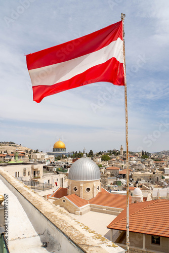 Waving Austrian flag in front of Jerusalem Old City as seen from Austrian Hospice. View at Church of Our Lady of Sorrows, Dome of the Rock on the Temple Mount and Al-Aqsa Mosque