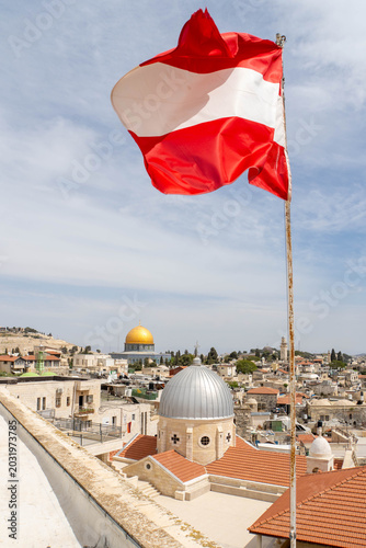 Waving Austrian flag in front of Jerusalem Old City as seen from Austrian Hospice. View at Church of Our Lady of Sorrows, Dome of the Rock on the Temple Mount and Al-Aqsa Mosque