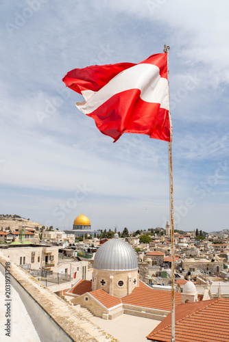 Waving Austrian flag in front of Jerusalem Old City as seen from Austrian Hospice. View at Church of Our Lady of Sorrows, Dome of the Rock on the Temple Mount and Al-Aqsa Mosque