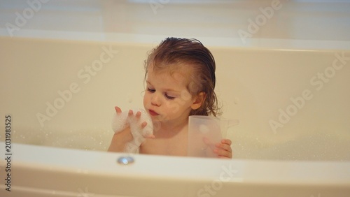 Toddler splashing joyfully in a bubbly bathtub, playing with soap and water during bath time, carefree childhood moment of hygiene, fun, and family bonding