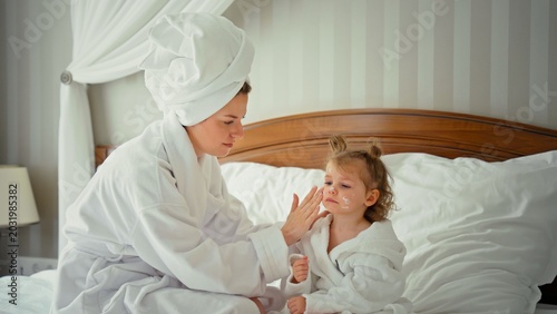 Photos Mother tenderly applies moisturizer to daughter's cheeks in bathrobes, a cozy mo