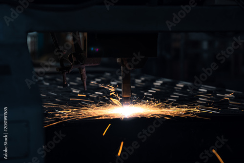 Extreme close up of automated cnc plasma machine cutting heavy steel metal plate with bright sparks. Smart industrial manufacturing technology and commercial corporate business production process.