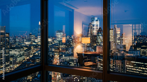 Empty office chair at desk overlooking illuminated city skyline at night with urban business district view