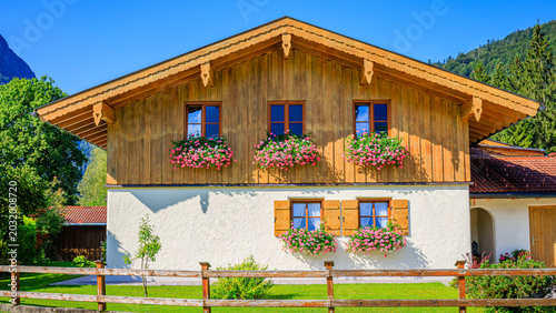 Quadro su tela Wooden house with flower boxes in a rural area of Germany under a clear blue sky