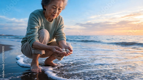 Senior Asian woman crouching on the shoreline holding seashells at sunset for seniors at the beach