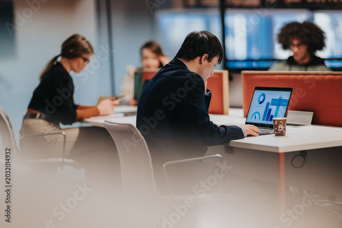 Foto Young professional focused on a laptop displaying charts while seated at a modern coworking desk