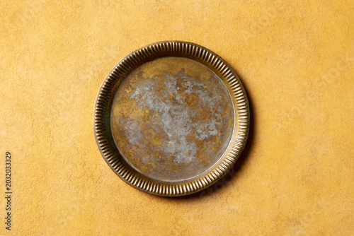 Rustic antique home decor platter. Handcrafted weathered metal dish on warm Mediterranean-style background for interior design. Ochre plaster textured wall, flat lay, copy space, top view.