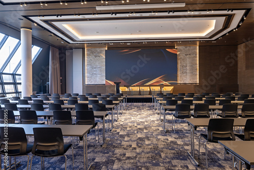 Empty modern conference hall with rows of tables and chairs facing the stage