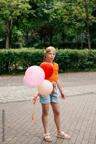 Blonde girl holding colorful balloons in park