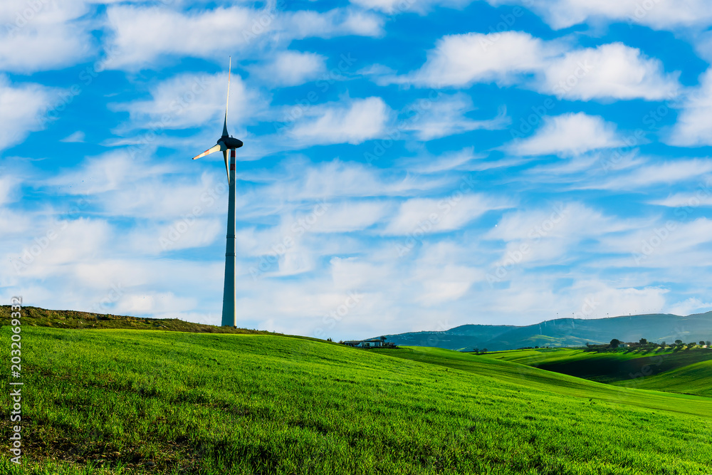 Obraz premium alternative energi power plant with wind turbine in a green summer field with hills and blue cloudy sky on background