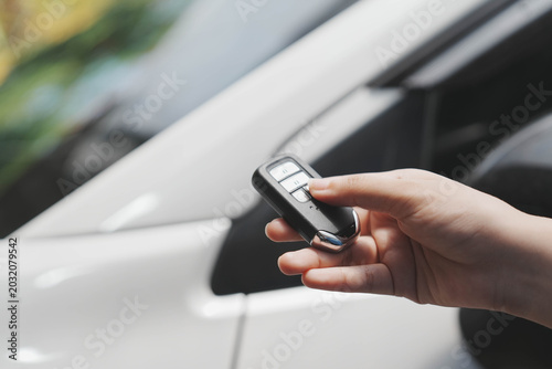 Foto Close-up of hand holding car key fob near white vehicle door, pressing remote button for locking or unlocking, shallow depth of field, modern transport and security concept