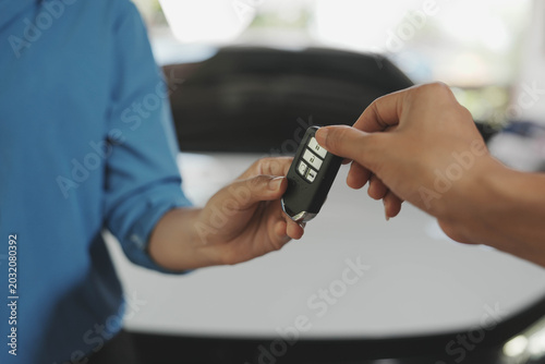 Photos Close-up of hands exchanging a car key fob outdoors near a vehicle, symbolizing car purchase, rental