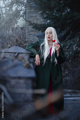 A gothic vampire with bloody hands and a mystical look drinks from a glass.
